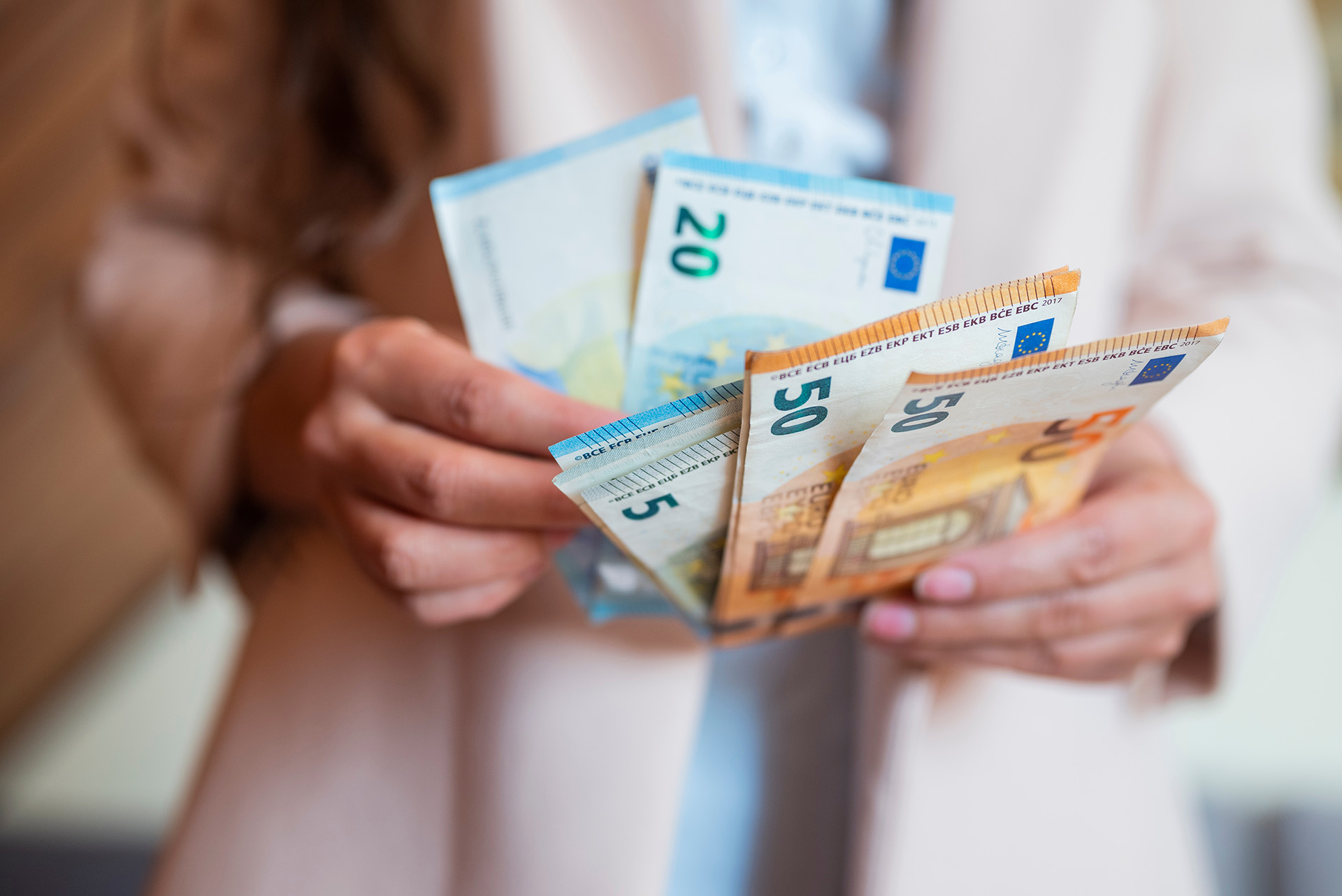 Eine Person, die mehrere Euro-Banknoten in der Hand hält und zählt, darunter 5-, 20- und 50-Euro-Scheine - ideal zur Veranschaulichung der baufinanzierung beratung bei Ihrer Immobiliensuche. Nur ihre Hände und ein Teil ihres Oberkörpers sind sichtbar.