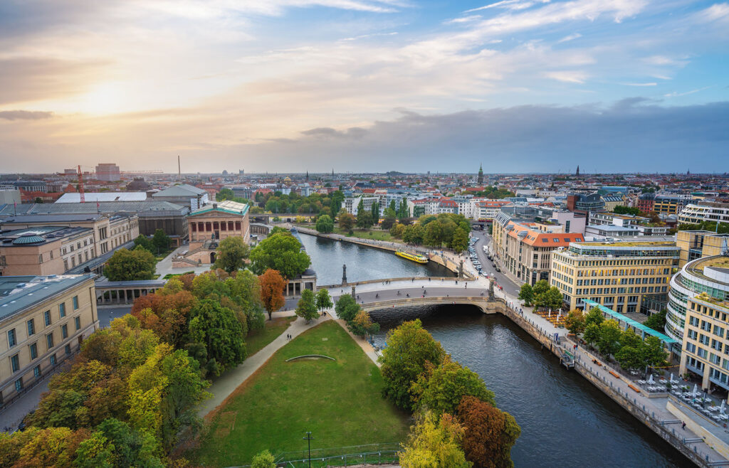 Luftaufnahme von Berlin bei Sonnenuntergang mit der Spree, den historischen Gebäuden der Museumsinsel, grünen Bäumen und dem Stadtbild bei bewölktem Himmel - ein atemberaubender Kontrast für alle, die Baufinanzierung in Dresden oder anderswo in Deutschland in Betracht ziehen.